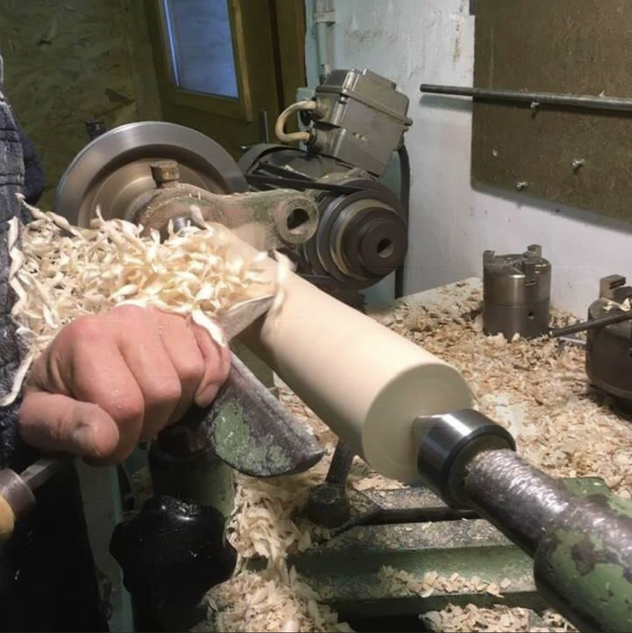 Hand mit Drechselröhre formt einen Holzzylinder auf der Drechselbank; Holzspäne fliegen